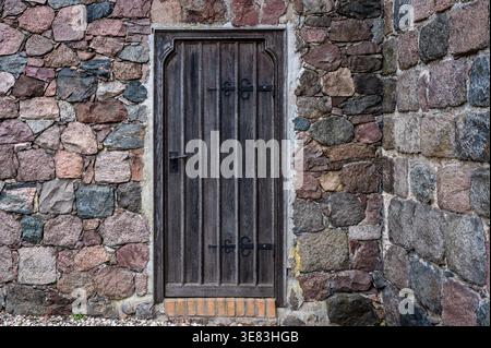 Historic wooden side door at the fieldstone church in Schwanebeck, Barnim, Germany. The dark vertical planks with metal bars. Stock Photo