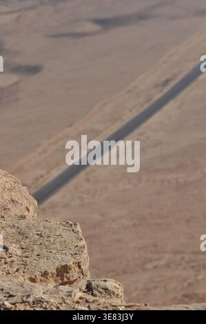 A rocky cliff offers a panoramic view of a long, winding road cutting through a vast desert landscape under a clear blue sky. The scene captures the b Stock Photo