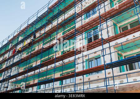 Construction workers are engaged in building a new structure. They are using scaffolding and working on the outer walls. The setting is an urban area Stock Photo