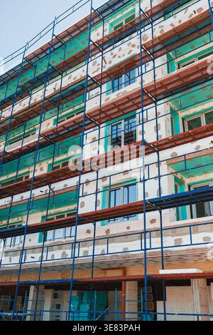Workers are seen on scaffolding as they work on the outer walls of a new building under construction. The process includes applying coatings and prepa Stock Photo