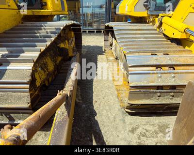 Bulldozers sit side by side on a construction site. The ground is dry and dusty. The machines have yellow paint and large metal tracks that show signs Stock Photo
