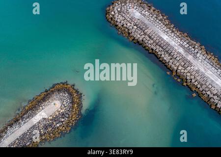Top down aerial drone view of a stone breakwater and jetty in a turquoise sea Stock Photo