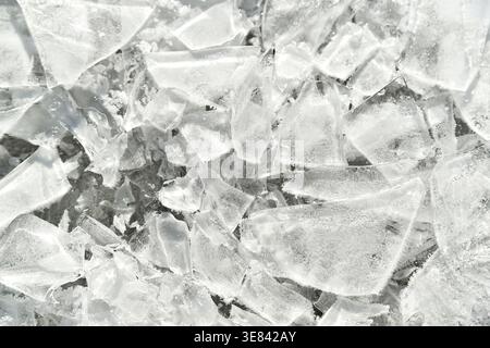 Broken ice shards lie scattered, sharp edges catching light. Crystalline fragments reflect brightness, creating icy texture. Stock Photo