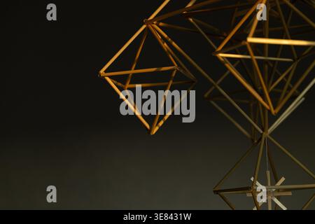 A golden geometric sculpture composed of interconnected triangles and lines on a dark gradient background, showcasing a 3D structure with metallic she Stock Photo