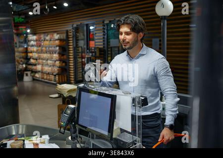 A man is standing in front of a computer display in a store, paying by his mobile phone Stock Photo