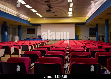 Empty conference hall or auditorium with red seats facing a projection screen, generic modern interior design. Stock Photo