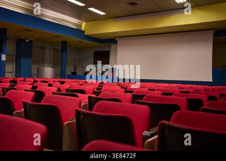 University auditorium with rows of empty red seats, a white projection screen, and conference hall interior in parma Stock Photo