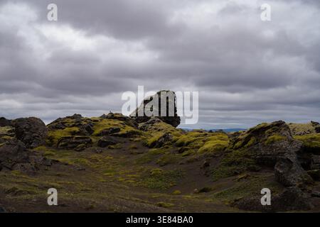 View of moss-covered volcanic rocks punctuate the stark landscape under a dramatic sky, where earth meets the heavens in a symphony of gray and green, Stock Photo