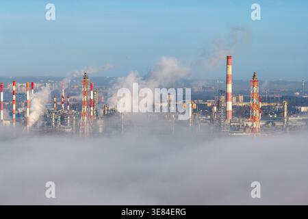 Aerial view of big refinery complex with tall chimneys releasing white smoke piercing through a sea of fog, Gdansk, Pomorskie voivodeship, Poland. Stock Photo