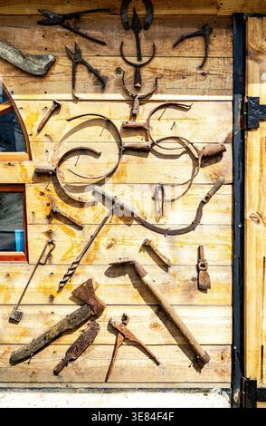 Assorted old rusty metal work tools on wooden wall. Vintage rusty household tools hang on the wall Stock Photo
