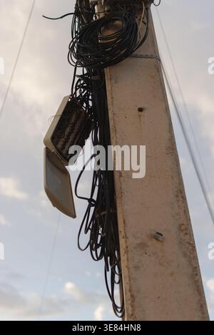 Utility pole overwhelmed by a chaotic network of electrical power lines and telephone cables. With an open distribution box revealing exposed wiring. Stock Photo