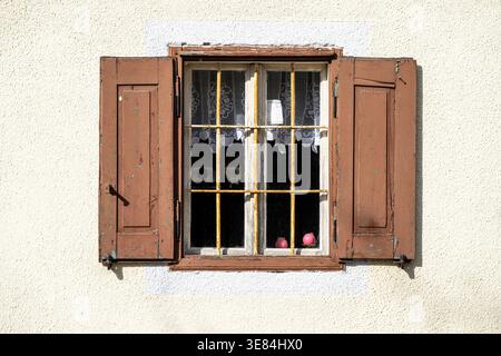 Two pink candles sit on a windowsill behind a barred window, framed by weathered brown shutters. The scene evokes a sense of quiet domesticity, perhap Stock Photo