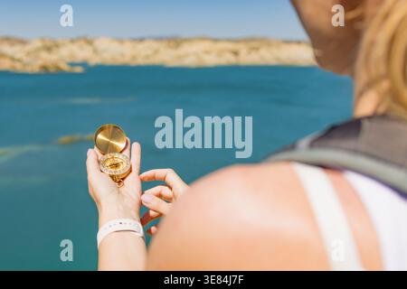 Traveler holding a vintage golden compass, navigating a journey and finding direction with exploration over scenic clear blue water and rocky desert l Stock Photo