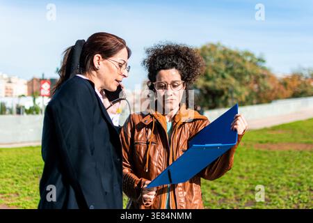 Businesswomen discussing outdoors, collaborating and communicating working document Stock Photo