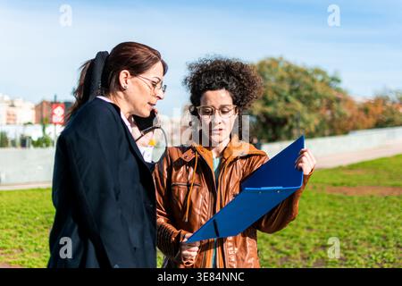 Businesswomen discussing documents outdoors while talking on phone Stock Photo