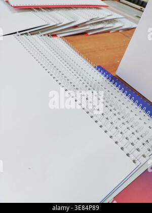 Stack of blank spiral notebooks with white pages and colorful covers arranged on a wooden table, showcasing various sizes and designs in a stationary Stock Photo