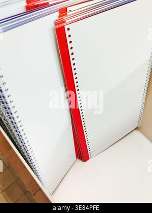 Stack of spiral-bound notebooks with blank white pages and a red cover, arranged neatly on a shelf in a stationery store Stock Photo