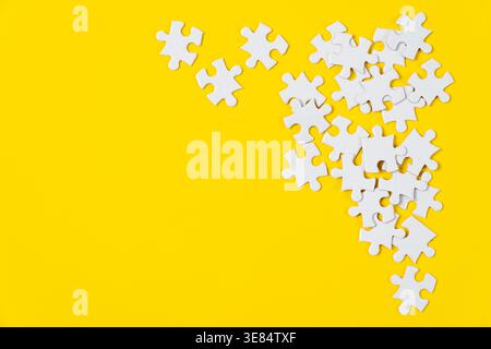 A top down view of several blank white puzzle pieces scattered across a vibrant yellow surface, leaving copy space on the left side for business theme or presentation template. Stock Photo