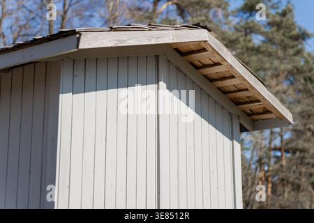 Small timber utility shed with weathered roof line and clean vertical cladding near trees, backyard structure, renovation and building exterior theme Stock Photo