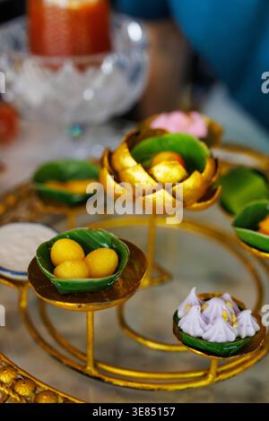Luxury afternoon tea set on marble table with ornate gold stand holding assorted bite-size desserts and fruit, with iced tea drinks and bokeh cafe bac Stock Photo