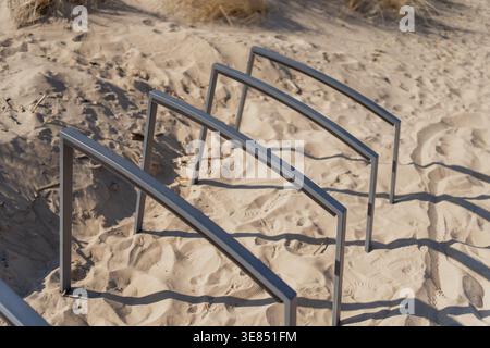 Beach access handrails set in sandy dune slope with footprints and dry grass, coastal infrastructure, pedestrian safety and seaside mobility concept Stock Photo