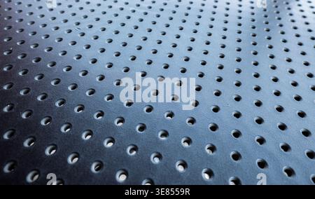 Macro view of a dark blue or black perforated metal sheet with a repetitive circular hole pattern Stock Photo