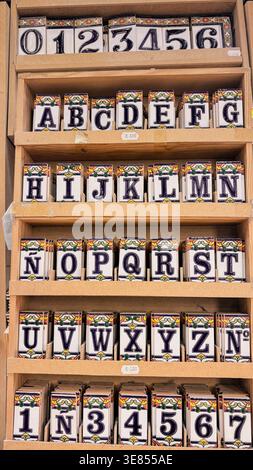 Andalusian ceramic alphabet tiles arranged on a rustic wooden shelf in warm Granada light (03-04-2026) Stock Photo