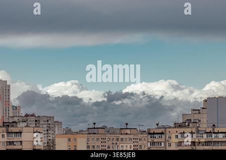 White and dark gray clouds against a clear sky and a big city. Dense, dark gray clouds hover above lighter, fluffy white clouds. Eastern Europe. Stock Photo