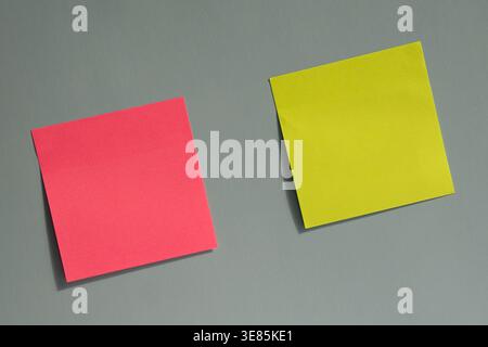 Horizontal image of two angled blank sticky notes, one pink and one yellow stuck on a light grey surface Stock Photo