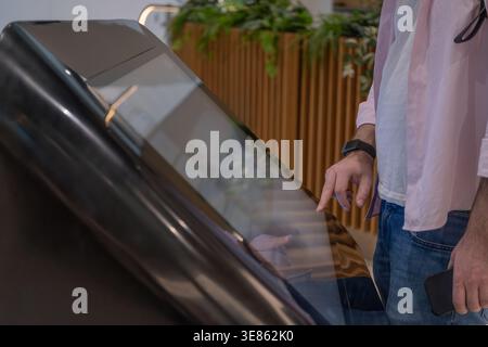 Close view of a man interacting with a touchscreen kiosk in a modern indoor environment. Concept of self service technology, digital interfaces, and c Stock Photo