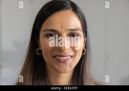 Indian woman smiling gently facing camera in studio with gold bindi, hoop earrings Stock Photo