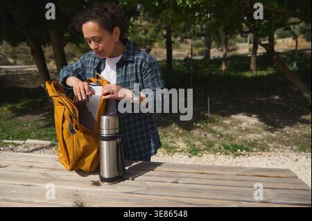 Freelance woman packing her laptop into a backpack after working outdoors in a park. Concept of mobile office, flexible work lifestyle and digital nom Stock Photo