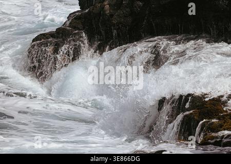 Powerful Atlantic waves crash over dark volcanic rocks, creating white foam and spray along the rugged coastline of La Palma island, Canary Islands, S Stock Photo
