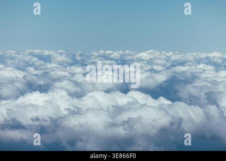 Serene aerial view of a vast sea of fluffy white clouds stretching to the horizon beneath a clear blue sky, creating a calm atmospheric background. Stock Photo