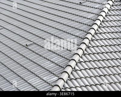 Close-up view of a grey ceramic tiled roof with ridge cap line and repeating wave pattern, creating a clean architectural texture background for const Stock Photo