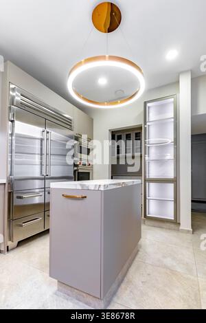 Luxury minimalist kitchen interior with sleek island and marble top, stainless steel appliances, and warm ring pendant lighting in a clean, modern hom Stock Photo