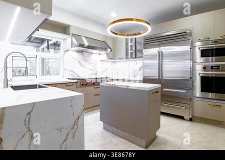 Bright luxury minimalist kitchen interior with marble countertops and backsplash, gray island, stainless steel appliances, and modern pendant lighting Stock Photo