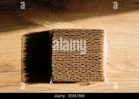 A detailed stack of rye crispbread sits on a wooden surface, casting a long shadow in soft lighting. Perfect for health-conscious snacks or a light me Stock Photo