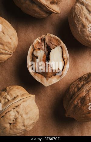 Macro close-up of a cracked walnut shell revealing the kernel, surrounded by whole walnuts on a rustic brown background. Natural food texture with war Stock Photo
