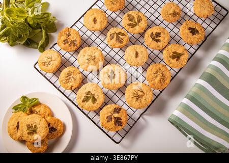 Freshly baked parmesan shortbread cookies topped with herbs displayed on a cooling rack. Delicate and savory, ideal for snacks or gourmet gifting. Per Stock Photo