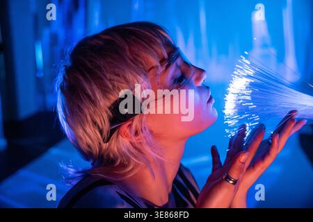 A young woman immersed in a futuristic setting, surrounded by glowing fiber optics, embodies the concept of the metaverse. The scene reflects innovati Stock Photo