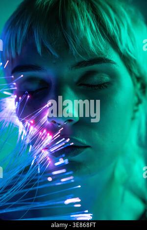 A young woman with closed eyes, surrounded by glowing fiber optics, embodies a futuristic look linked to the metaverse, highlighting a blend of techno Stock Photo