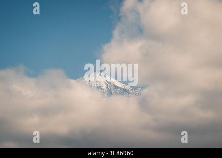 Snow-covered peak of Mount Teide emerges through clouds, set against a clear blue sky on a serene winter day in Tenerife, showcasing the island's natu Stock Photo