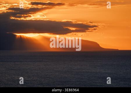 Captivating winter sunset over the Tenerife coast, with the sun casting golden rays through dramatic clouds, showcasing the island's natural beauty an Stock Photo