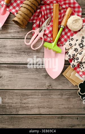A collection of gardening tools on a wooden table, featuring a mini shovel, rake, scissors, and twine. Ideal for spring planting, set on a checkered c Stock Photo