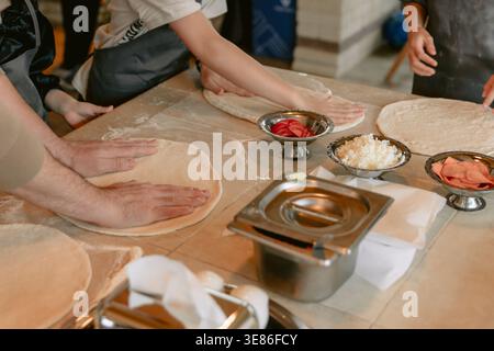 Hands preparing pizza dough with fresh ingredients in kitchen cooking class or restaurant Stock Photo