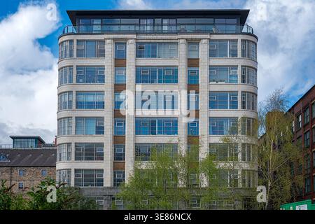 Modern residential building featuring a distinctive curved facade with many windows, standing against a blue sky with white clouds in the vibrant manc Stock Photo