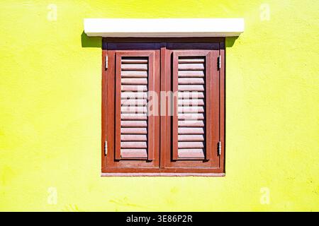 Minimalist architectural detail featuring brown wooden shutters on a vibrant lime yellow wall with white cornice in bright sunlight Stock Photo