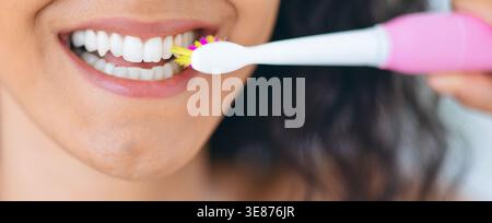 Woman Brushes Teeth With Electric Toothbrush in Bathroom During Morning Routine Stock Photo