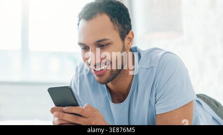 Young Man Smiles While Using Smartphone at Home During Daytime Activity Stock Photo
